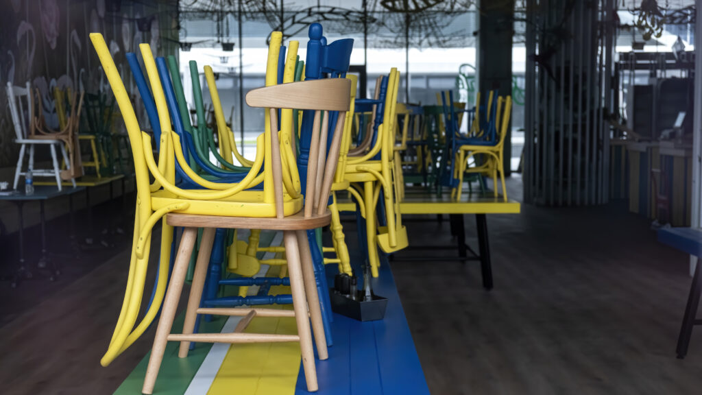 “Stacked colorful wooden chairs placed upside down on tables inside a closed modern café with glass walls.”