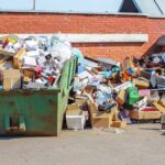 Overflowing dumpster filled with cardboard boxes and trash behind a building, illustrating Junk removal services kent wa for commercial waste cleanup.